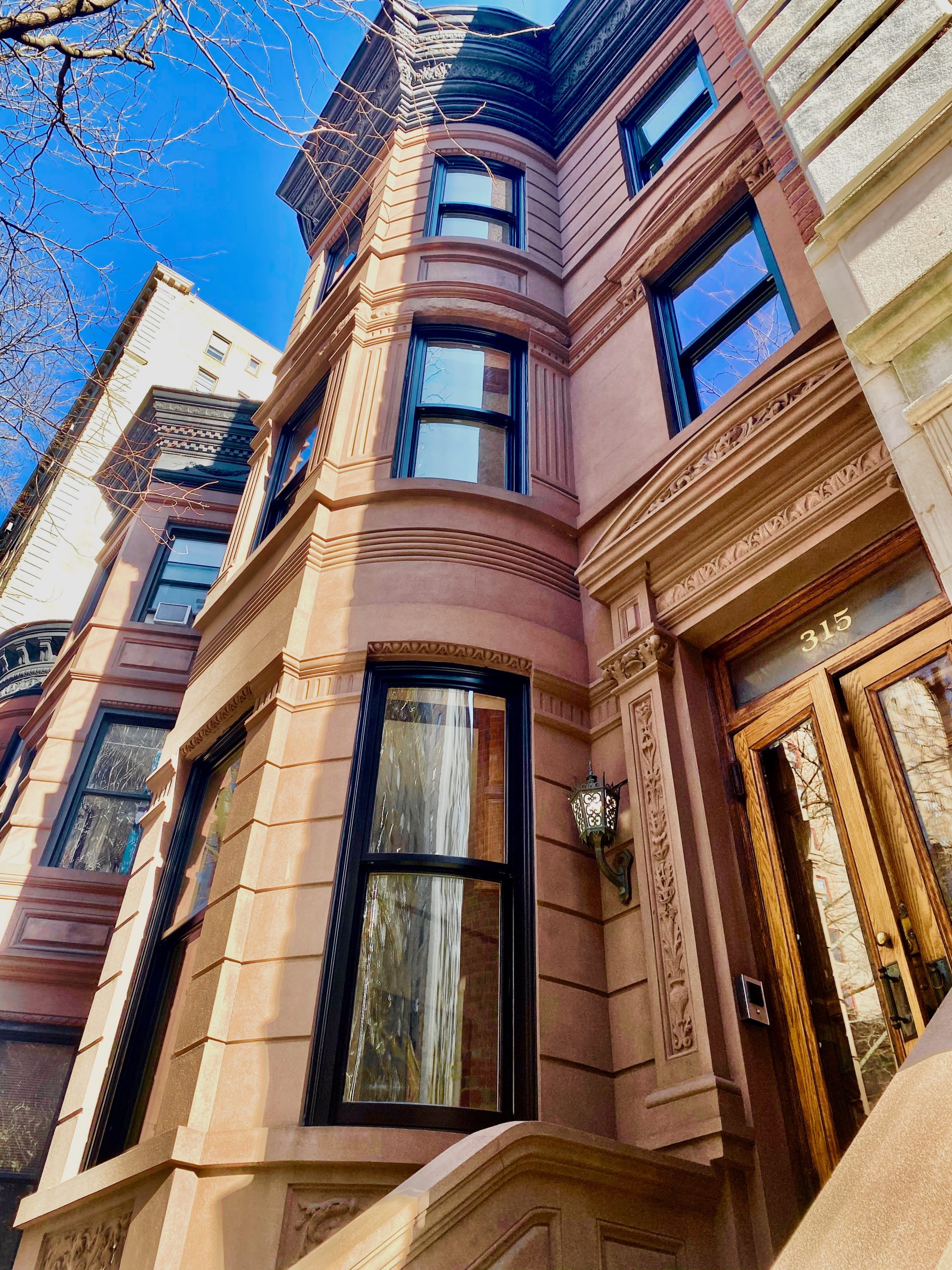 Exterior view of a historic brownstone building featuring large windows and intricate architectural details, with a wooden front door and elegant lighting.